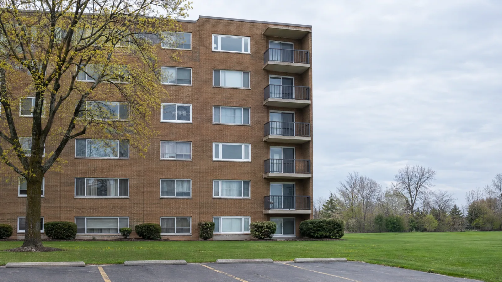 1960s brown-brick apartment building with a patchwork of older aluminium sliders and newer white vinyl slider windows