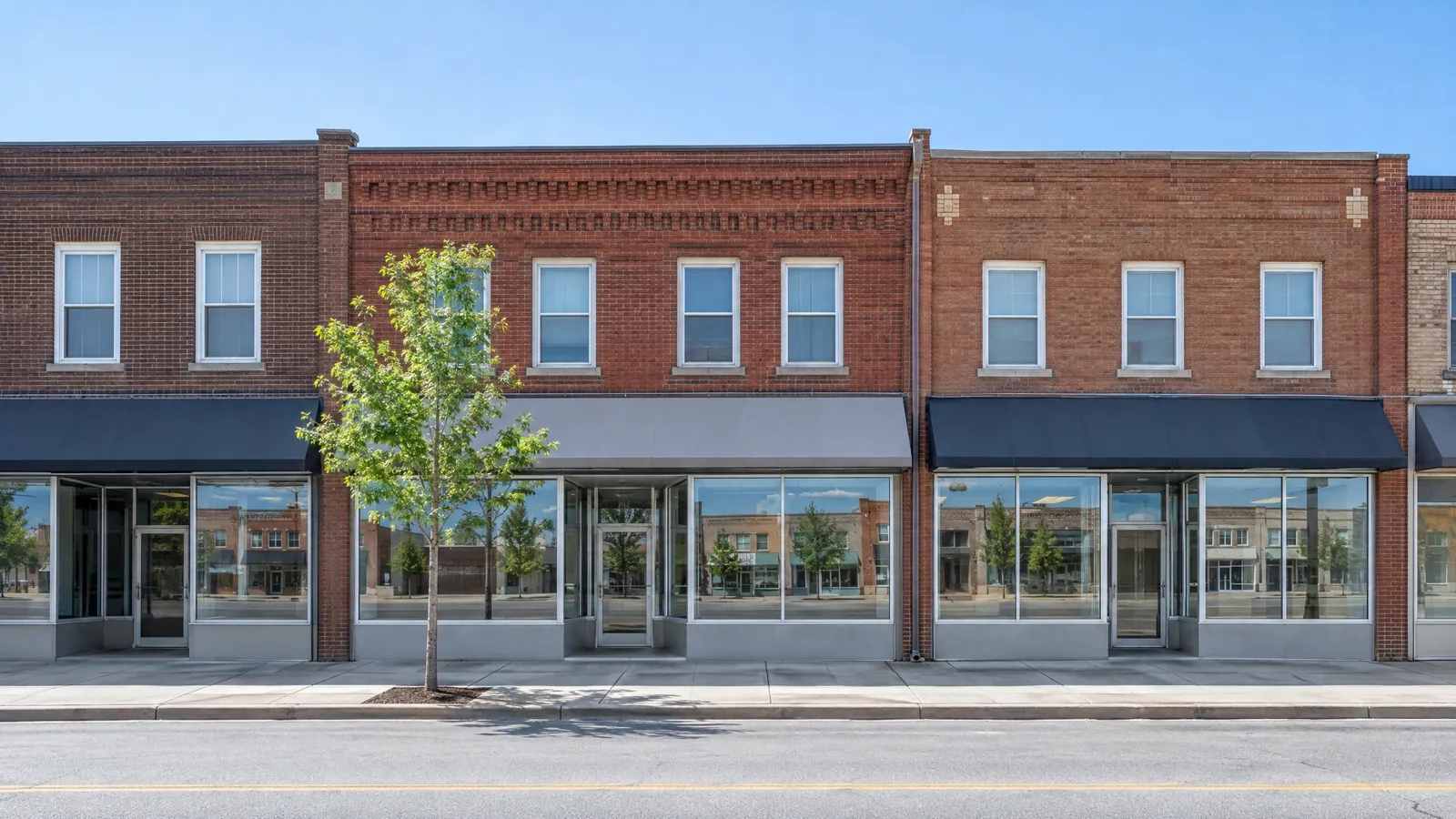 Row of two-storey brick commercial buildings with wide ground-floor display windows and smaller windows upstairs, on a quiet main street